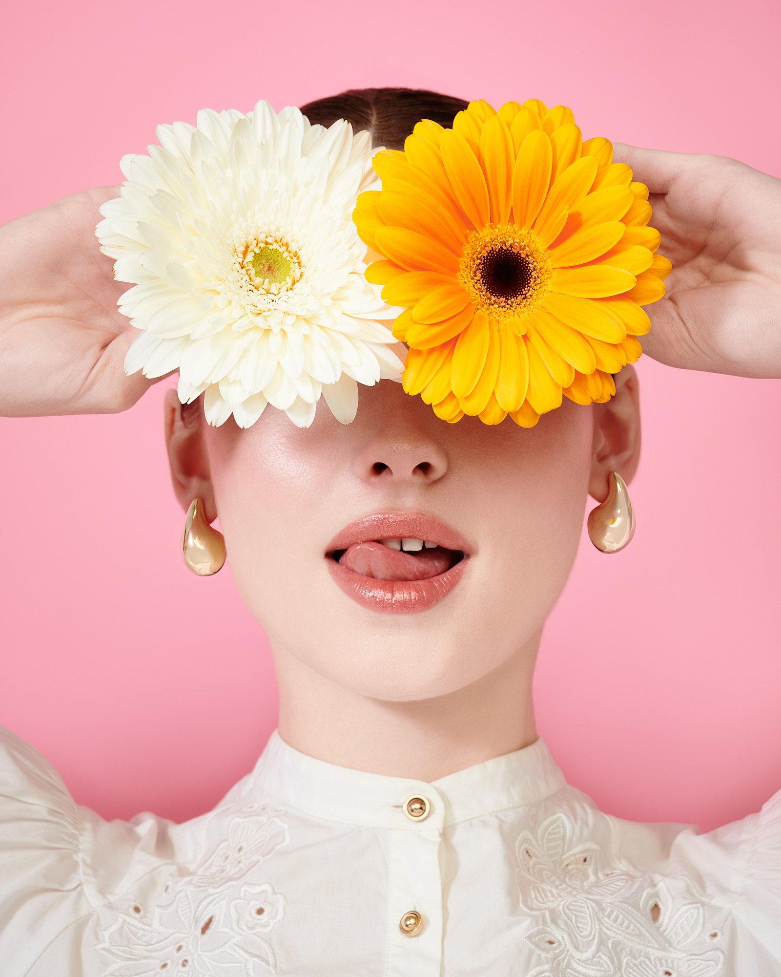 Modella con fiori sugli occhi e orecchini d'oro su fondo rosa
