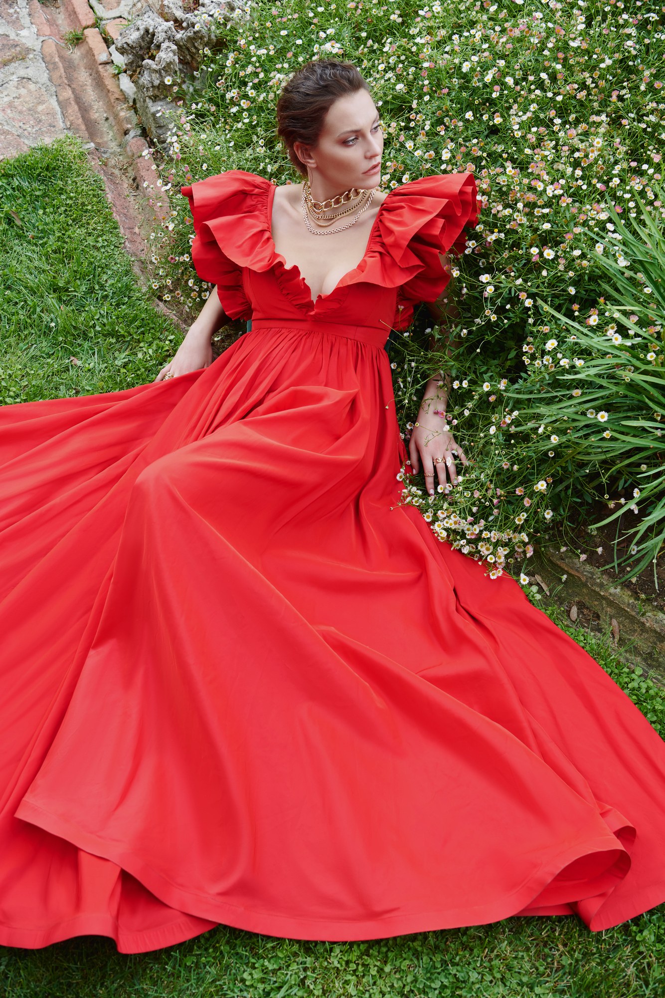 Modella in abito rosso con collana d'oro sdraiata in giardino