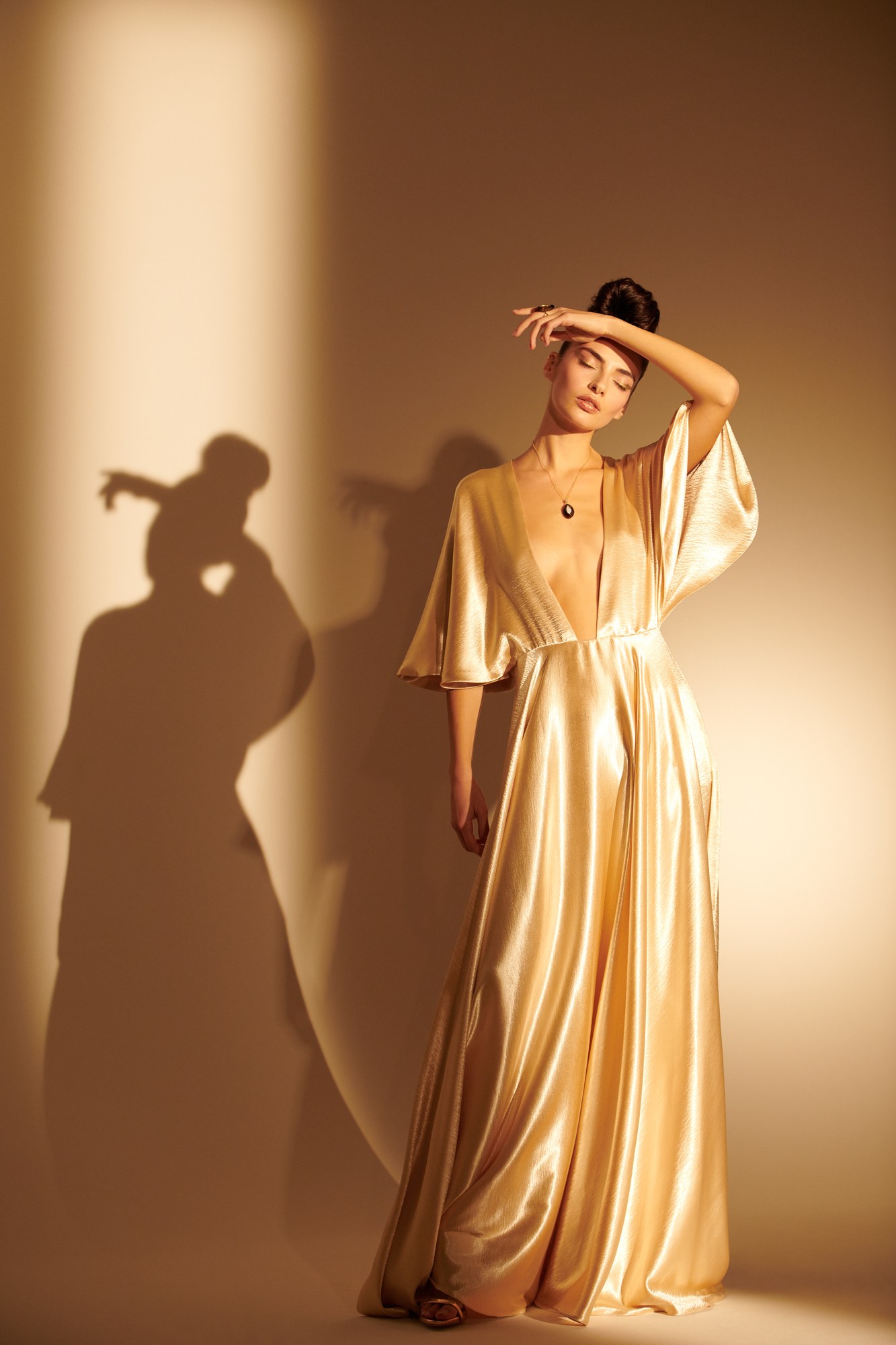 Modella in abito dorato con ombra su parete calda