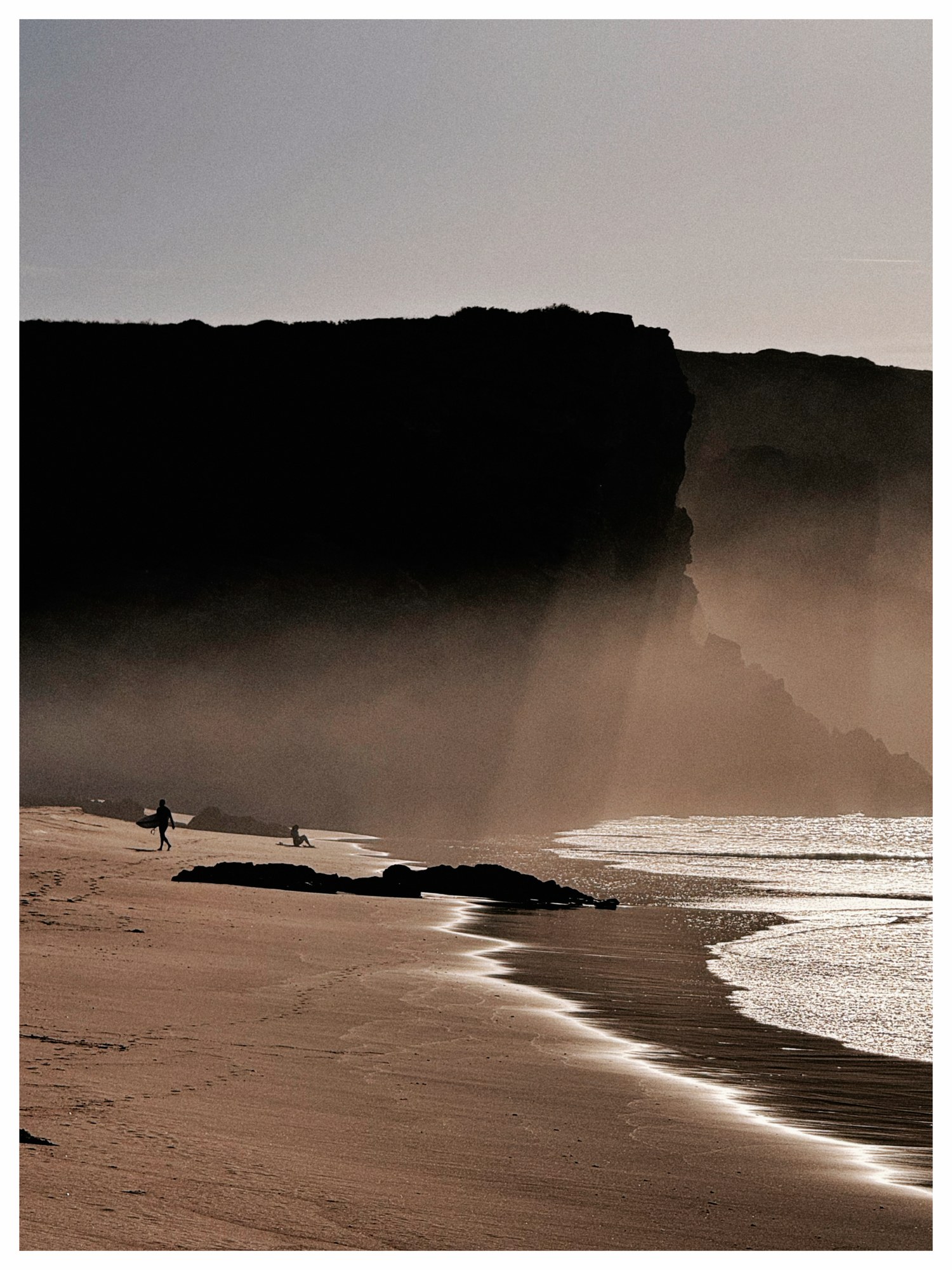 Scogliera e spiaggia nella nebbia al tramonto con un surfista