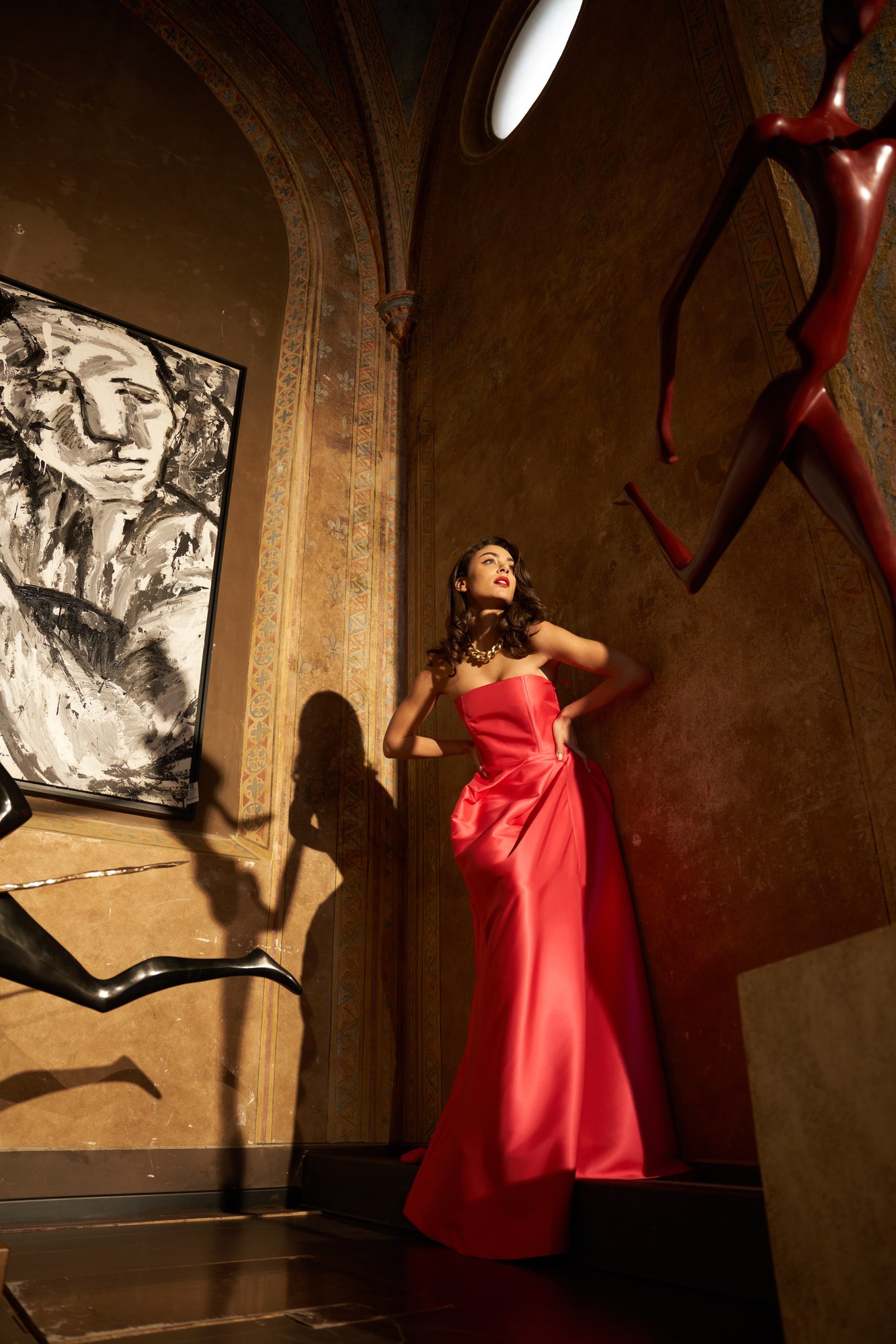 Modella in abito rosso in un palazzo storico con sculture, Luisa Via Roma