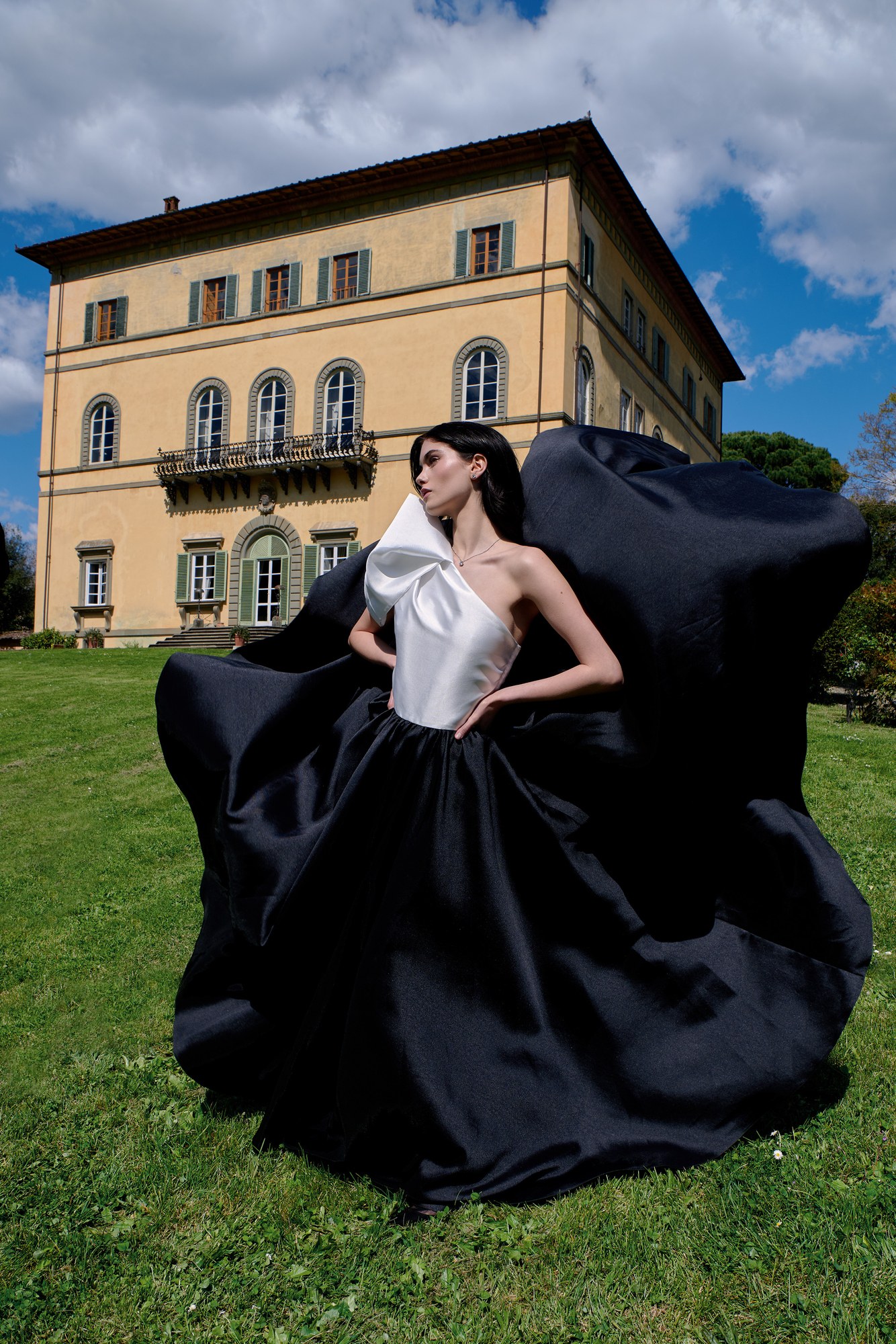 Modella con gonna nera voluminosa sul prato davanti a una villa toscana