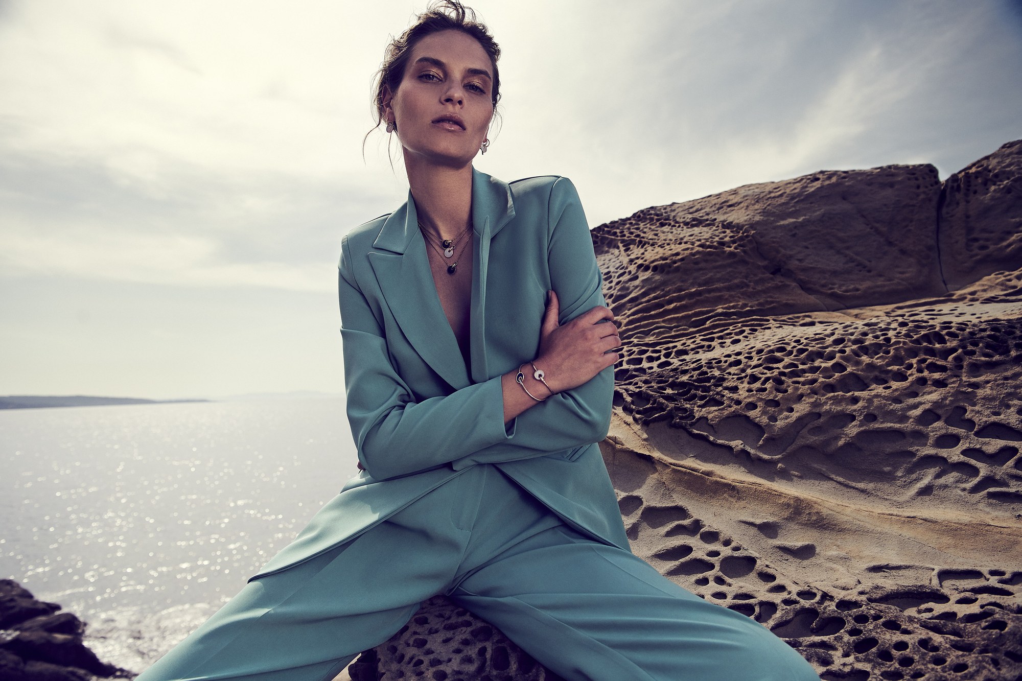 Modella in completo verde menta seduta sulle rocce sul mare