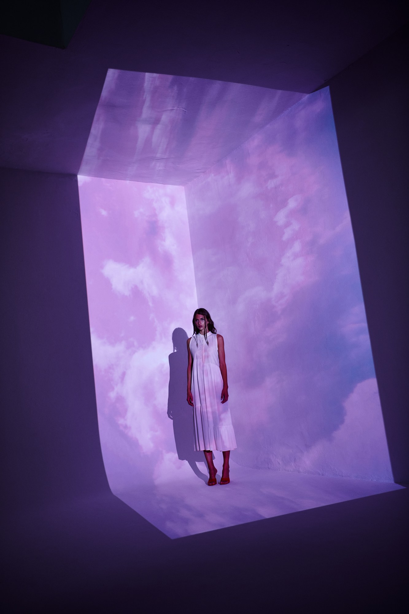Modella in un cubo di luce con nuvole viola proiettate