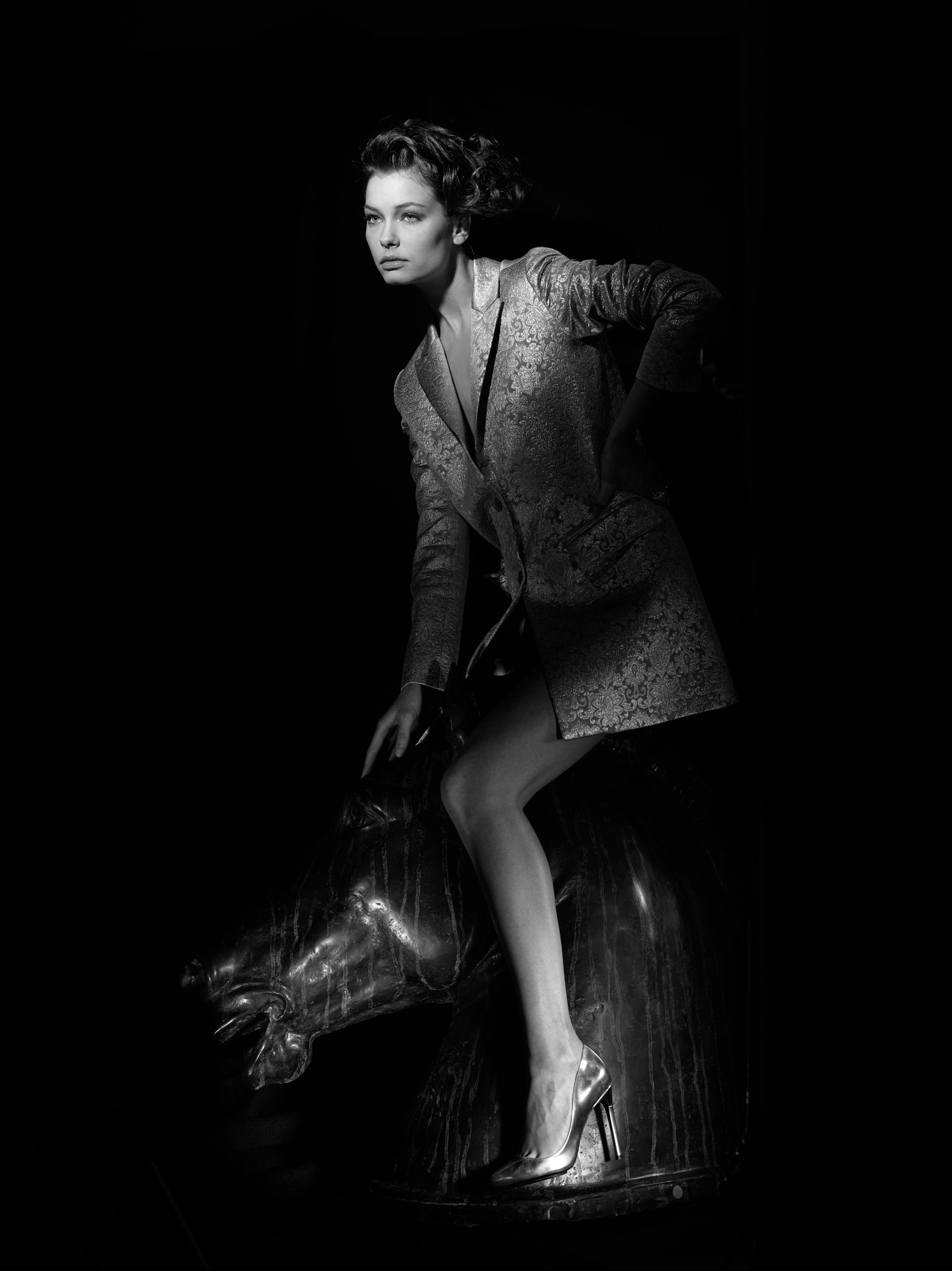 Modella in tailleur argento su una scultura di cavallo, bianco e nero