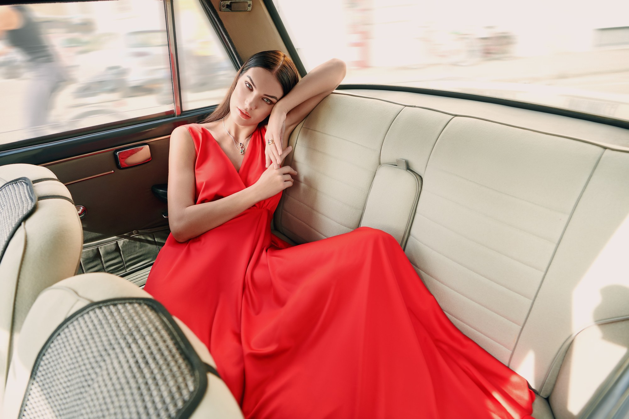 Modella in abito rosso sdraiata sul sedile di un'auto d'epoca, editoriale moda