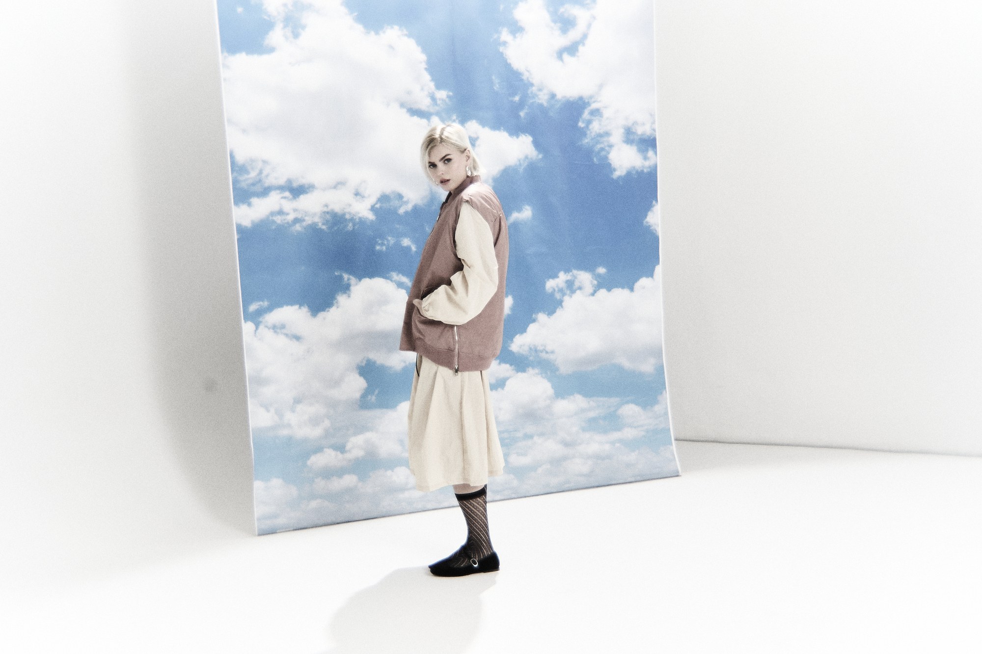 Modella in studio davanti a un pannello di cielo con nuvole