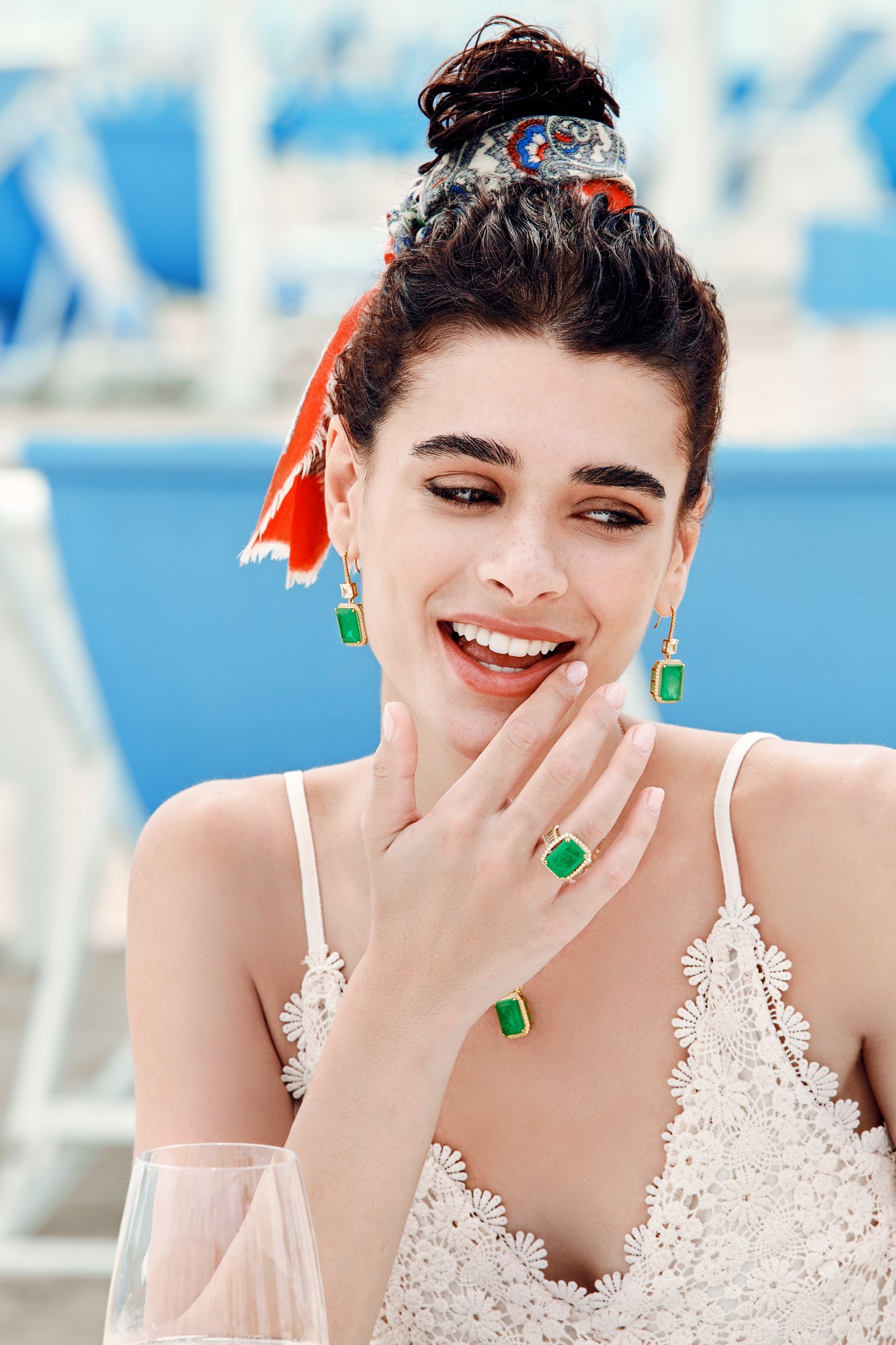 Modella sorridente con anello e orecchini di smeraldo a bordo piscina