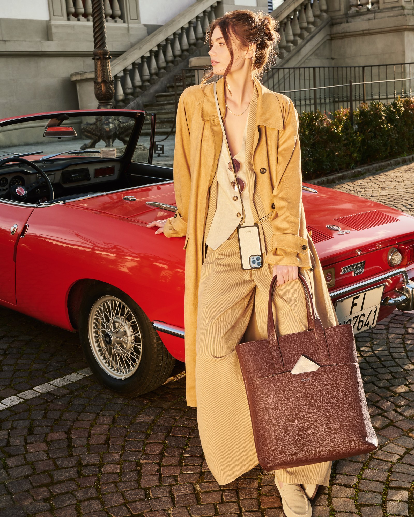 Modella con trench e borsa tote accanto a una spider rossa