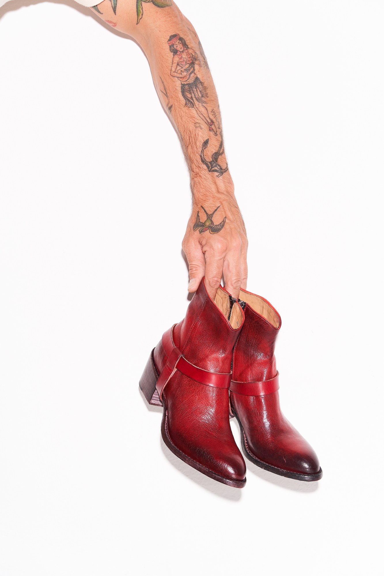 Mano tatuata che regge stivaletti in pelle rossa