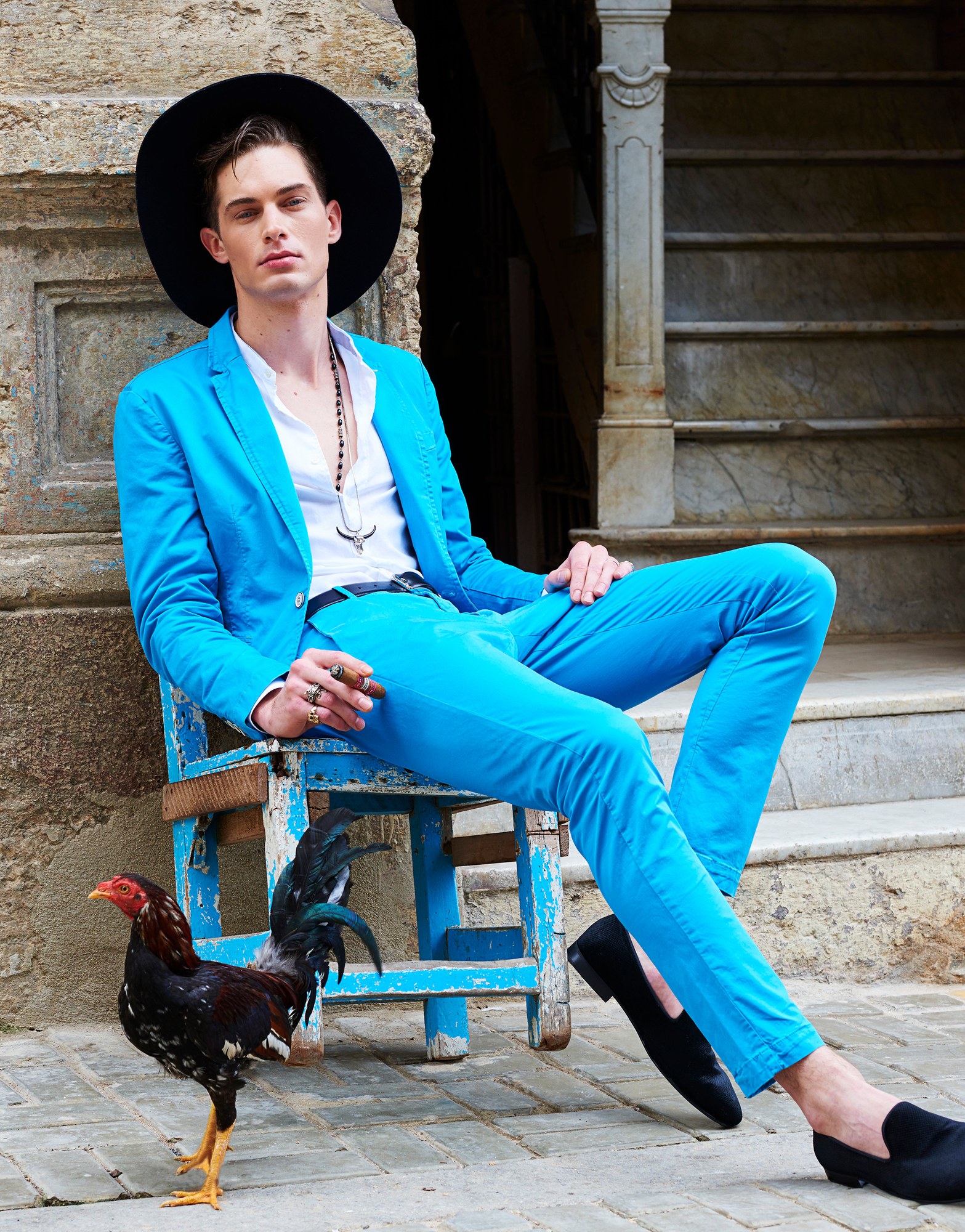 Modello in abito azzurro con cappello e un gallo su una scalinata in pietra