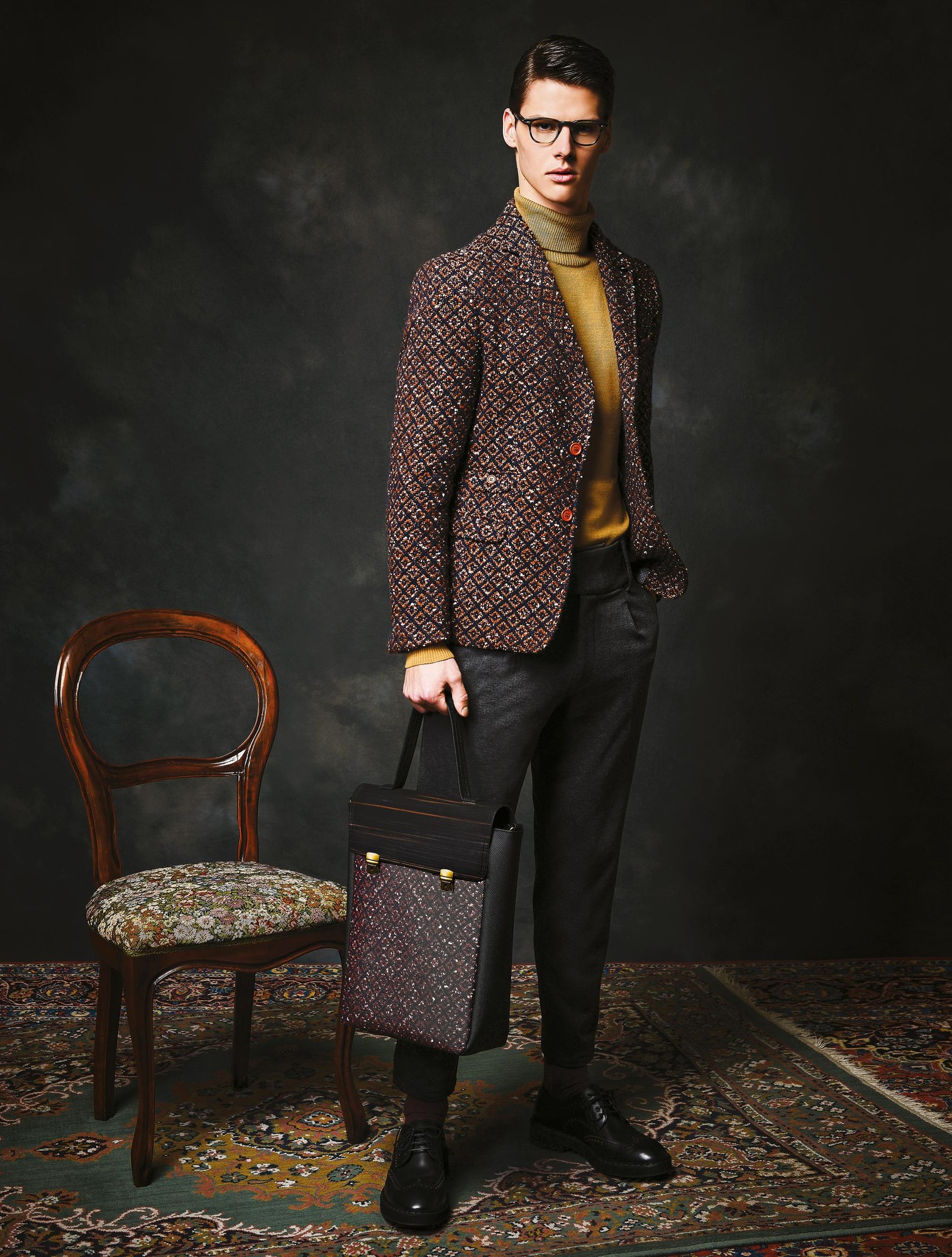 Modello in giacca tweed con borsa accanto a una sedia antica