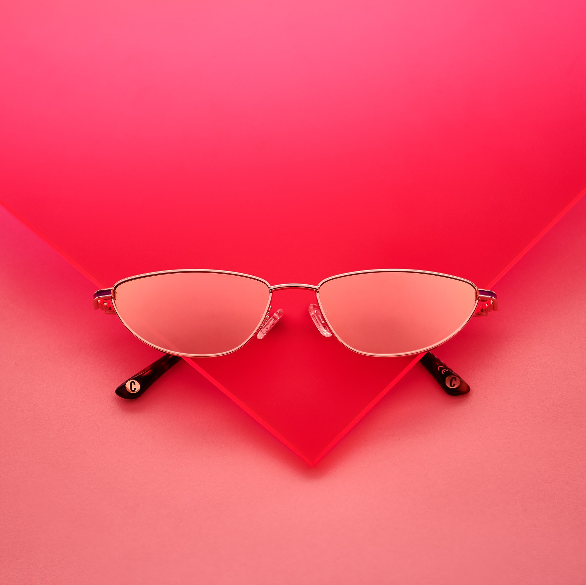 Occhiali da sole con lenti rosa su fondo rosso e rosa