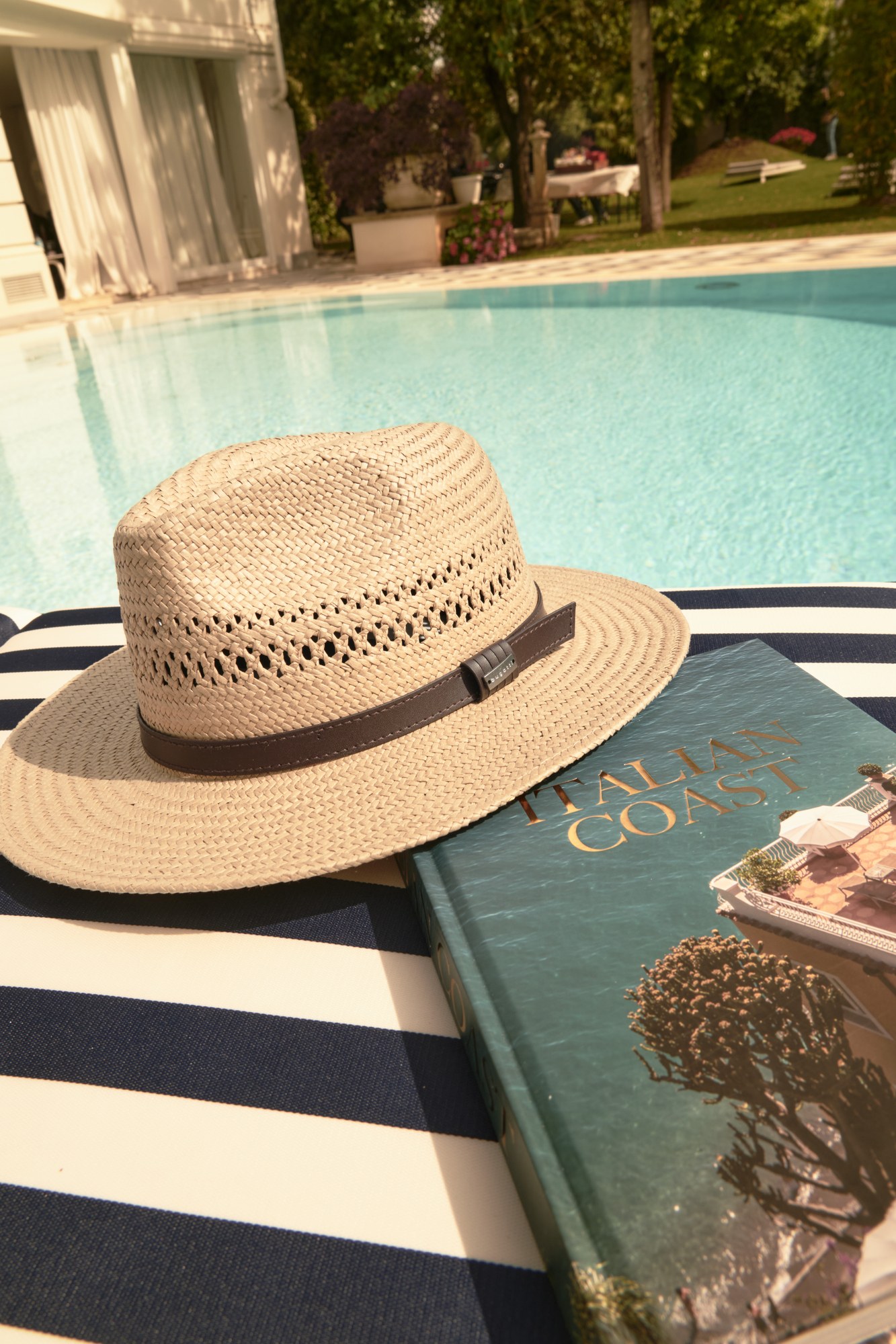 Cappello di paglia e libro su telo a righe a bordo piscina